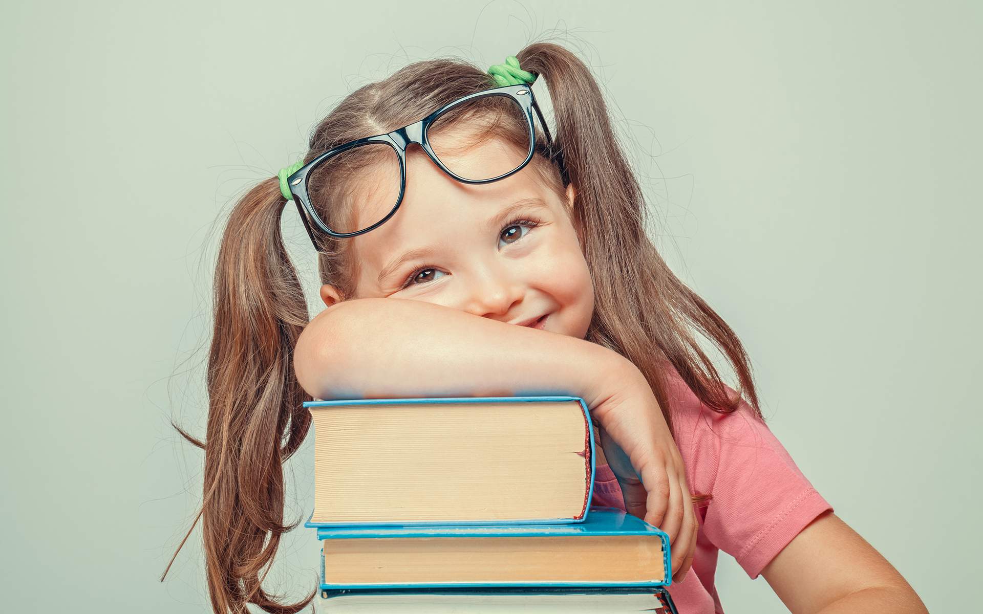 7 Classic Children’s Books that Teach Kids Mindfulness -Smiling beautiful cute little girl leaning on thick books