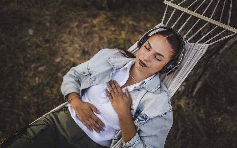 Photo of a young woman relaxing in a hammock with her hands resting on her chest and her belly and her eyes closed