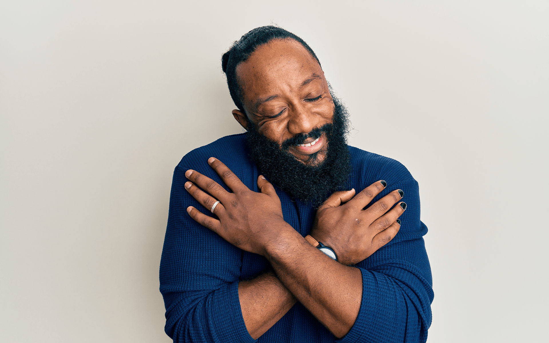A 12-Minute Meditation to Remind Yourself That You Are Enough—A Black man with a beard and a dark blue shirt on gives himself a hug.