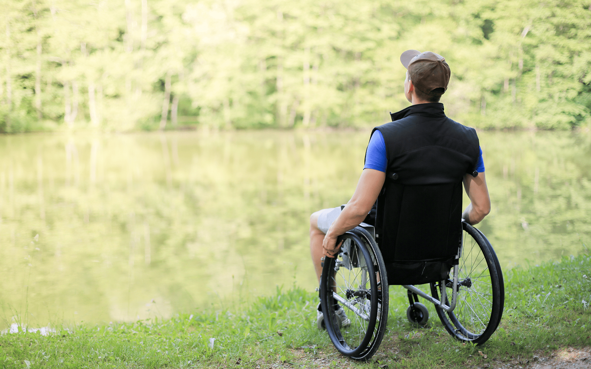 A Quick Tip to Take Your Mindfulness Practice Outside—A young white man in a wheelchair faces a lake with green trees around it.